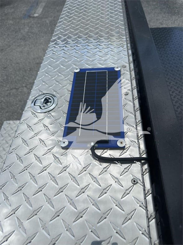 Solar panel with cable on a diamond plate flatbed surface; round recessed fuel cap or access port nearby.