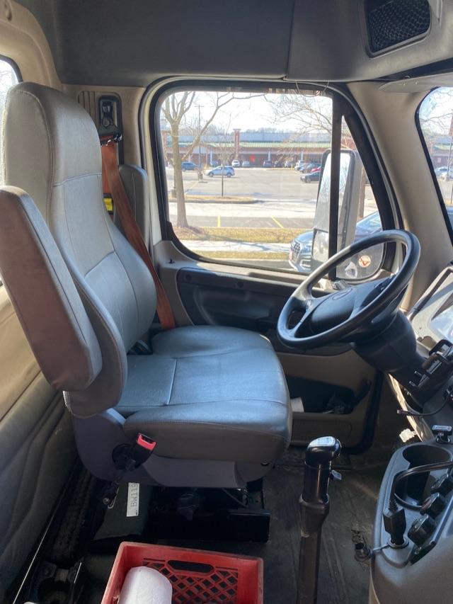 Interior of a Freightliner Cascadia cab showing driver seat, steering wheel, dashboard, gear shifter, and side window.