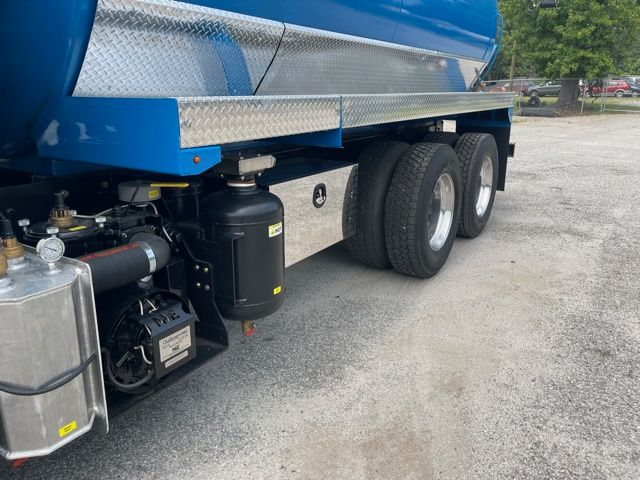 Freightliner Cascadia truck chassis side showing dual rear axles, blue tank, diamond plate side panels, and hydraulic components.