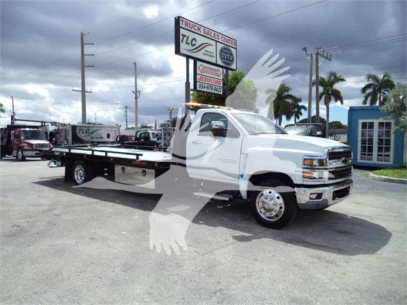 2023 Chevrolet Silverado 6500HD a white tow truck on a lot with a long flatbed; visible text on sign reads TLC Truck Sales Center and EVTI logos; license plate area not legible.