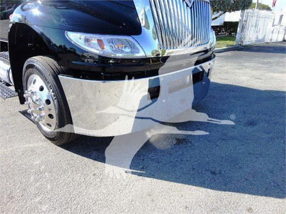 Truck front view showing chrome grille, bumper, and left front wheel of a new 2022 International MV tow truck with reflective surface.