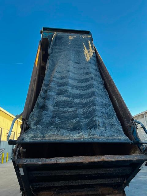 Dump truck bed from side, blue interior with wear marks and metal frame visible.