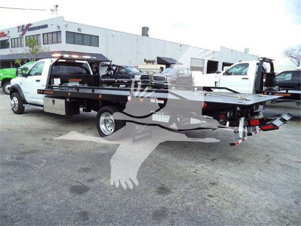Ram 5500 tow truck with flatbed, side view showing equipment and dealership background.