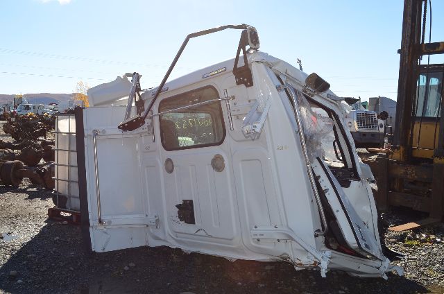 Cabover truck cab body in white showing side door, window, and mounting hardware; visible frame and rear panel; miscellaneous components and surrounding yard.