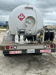 Rear of a tanker truck on a flatbed trailer showing circular tank with hazardous material placard 1075 and rear lights.