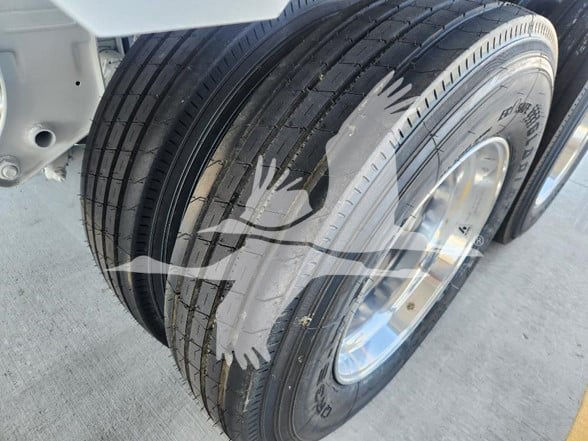 Trailer dual-axle wheel close-up showing tires and rim with visible tread; watermark graphic overlay across image.