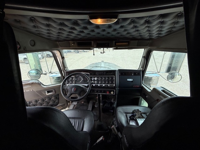 Kenworth W900 truck cabin dashboard view from driver seat with quilted ceiling and dual sun visors.