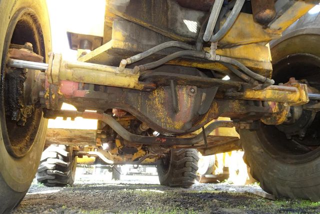 Axle view of a Grove RT58 crane undercarriage showing drivetrain and suspension components with yellow paint and dirt, front wheels on both sides.