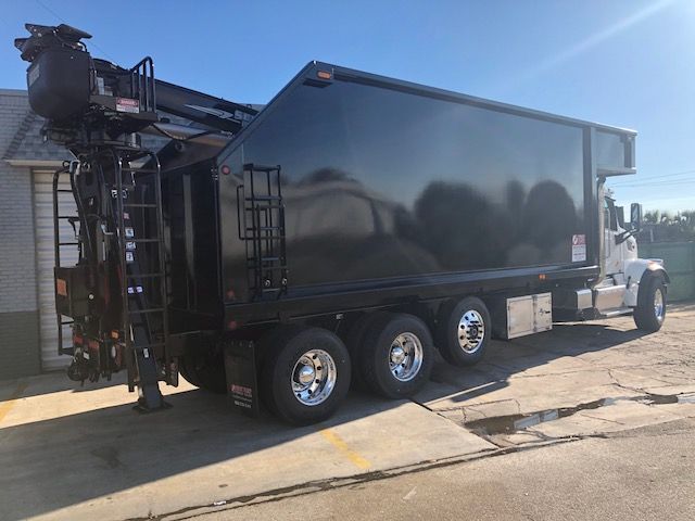 Peterbilt 567 grapple truck with a large black dump body and a mounted crane at rear.