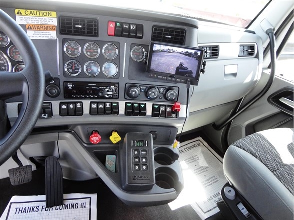 Dashboard and control panel of a 2022 Kenworth W900 truck showing steering wheel, gauges, a mounted display, various switches, and a gear/selector with cup holders.