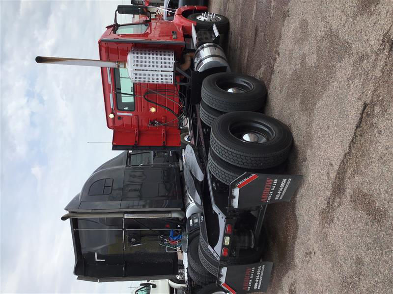 Conventional daycab tractor tractor with red cab and black sleeper, multiple wheels stacked near the cab, various hoses and exhaust stack visible.