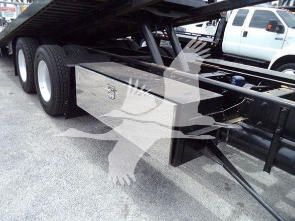 Flatbed truck chassis with dual rear tires and a silver tool/storage box mounted beneath the frame.