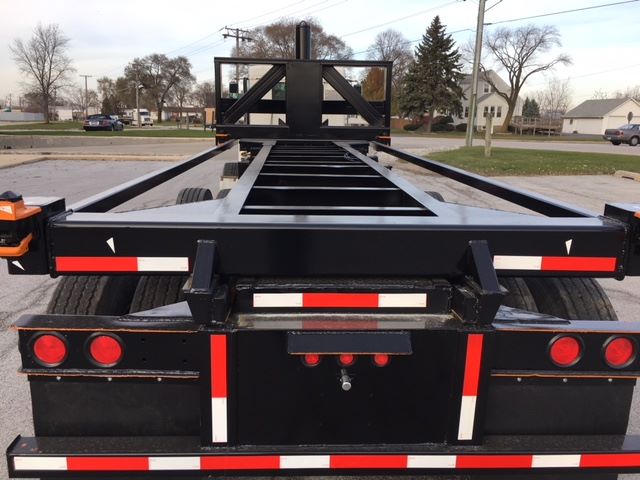 Rear view of a black flatbed trailer frame with red and white reflective tape, taillights, and a gooseneck-type hitch visible.