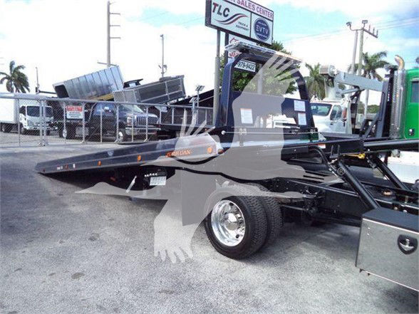 2023 International CV tow truck with flatbed, side view showing hydraulic arms and wheel, VIN and stock number visible in background.