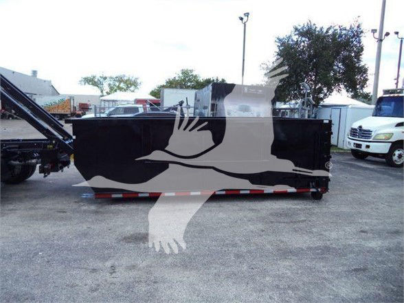 Image of a black refuse truck dumpster trailer with a white Ford F-550 in a yard, behind a logo watermark.