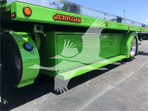Green Peterbilt 337 tow truck trailer side with 'JERR-DAN' logo in orange letters on a black oval, circular reflectors, and hinged compartments along the side.