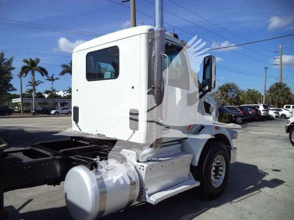 Peterbilt 567 tractor cab side view showing white exterior, fuel tank, steps, and rear fender against a dealership lot.