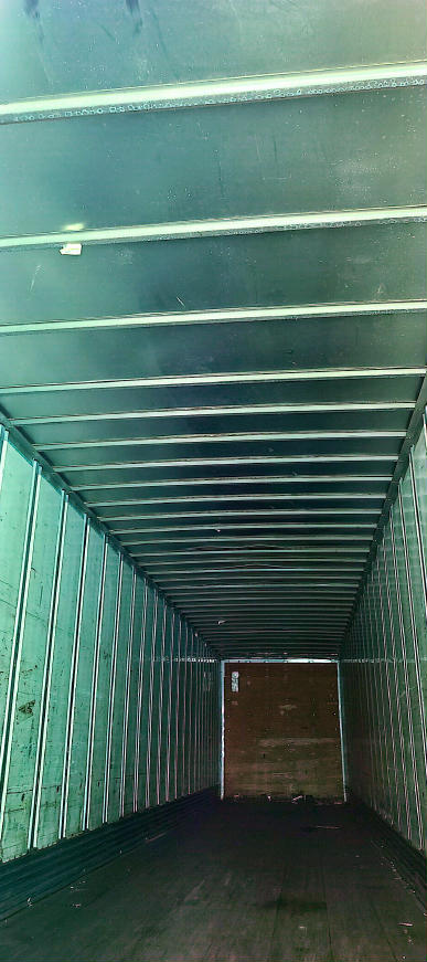 Interior of a utility trailer with ribbed metal walls and ceiling, showing a wooden floor at the far end.