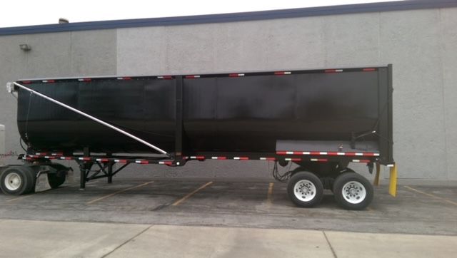 2009 Great Dane 40 ft round bottom dump trailer side view showing black body, dual axles, white wheels, and red-white reflective safety stripes.