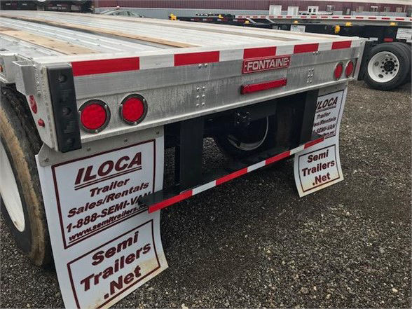 Flatbed trailer rear view showing Fontaine logo, reflective red/white stripes, taillights, and signage for ILOCA and Semi Trailers Net.