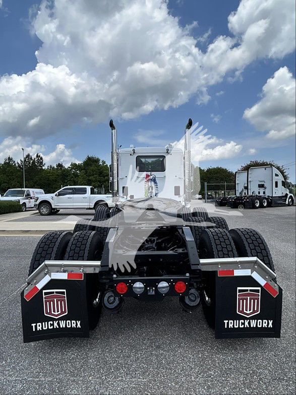 Kenworth T880 truck chassis rear view showing dual fifth wheel, dual rear axles, mud flaps with TruckWorx logo, white cab in distance.