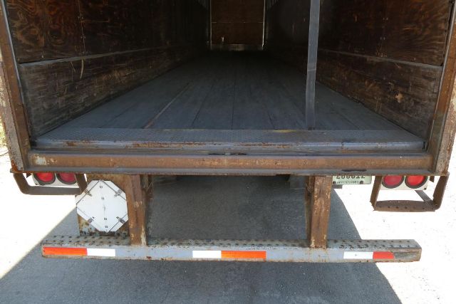 Trailer rear view showing open cargo area with wooden interior and rear bumper, tail lights, and step/fender.