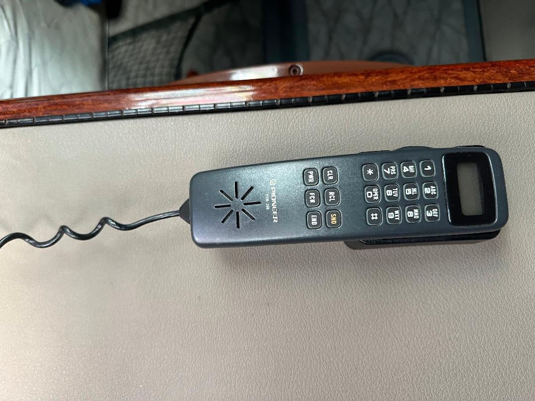 In-cab remote control device with numeric keypad and small display sitting on a beige dashboard edge; cord trailing off to the left.