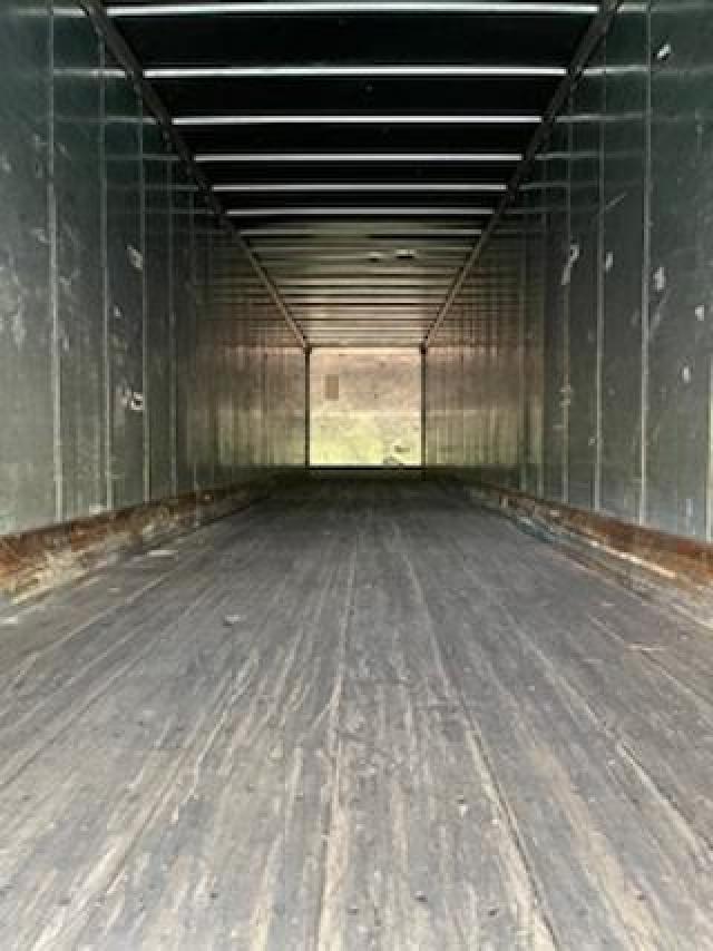 Inside trailer cargo area showing empty dry van with metal walls, wooden floor, and rear door at far end.