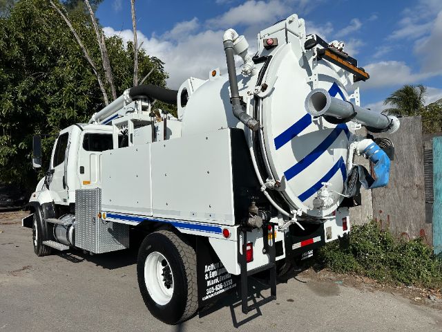 Freightliner 108SD vacuum truck side and rear view showing large vacuum tank with blue striped design, twin rear wheels, hoses and ladder.