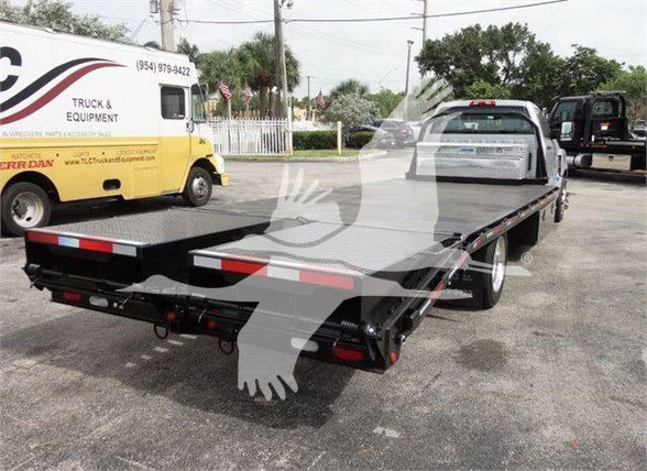 Flatbed truck bed of a 2023 Chevrolet Silverado 6500HD with a black steel deck, two rear ramps, and towing lights visible.