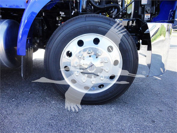 Front wheel of a blue Peterbilt truck with polished steel rim and tire, engine bay exposed in background.