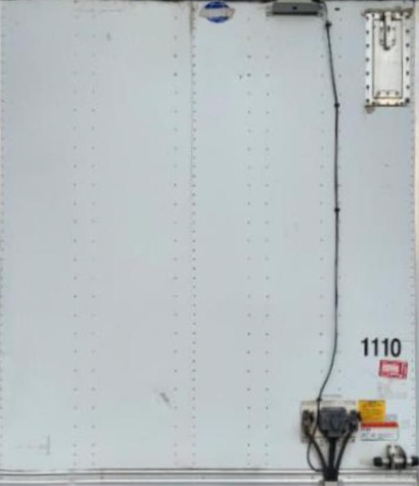 Trailer side with serial/stock markings: number 1110 near bottom right, electrical outlet and cables, warning sticker, riveted aluminum panels.
