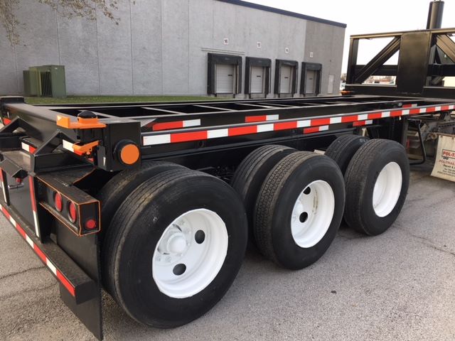 Trailer axle group with three axles and white rims, black/tinted tires, orange safety hardware, and red/white reflective tape along the side. Wabash tipper trailer visible in background.