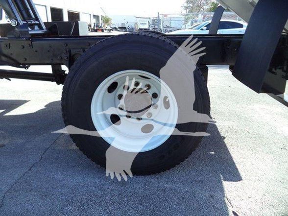Truck chassis showing a white wheel rim and a tire with a blue sky and yard in background. Overlay watermark of a bird/logo covering center.