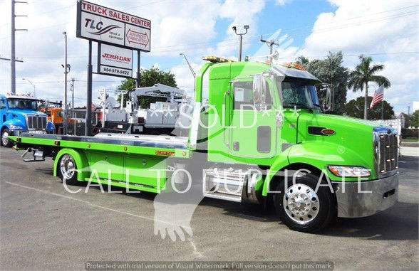 Green Peterbilt 337 tow truck in a dealership lot, side view with chrome front bumper and flatbed, TLC dealership signs in background.