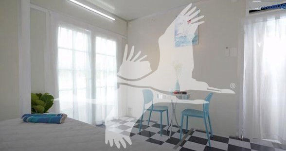 Interior of a small trailer with a bed, checkered floor, and a table with two blue stools; watermark of a large bird in flight overlaps the image.