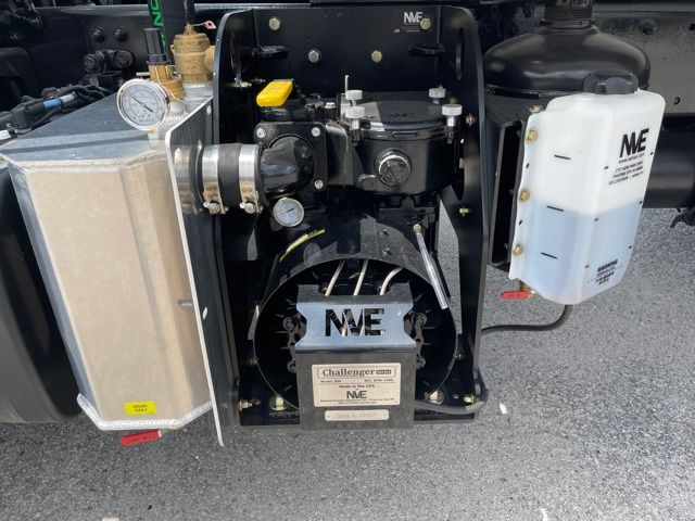 Front view of a Freightliner M2 auxiliary equipment: NVE Challenger engine with display plaque, white reservoir on right, radiator on left, various gauges and controls.