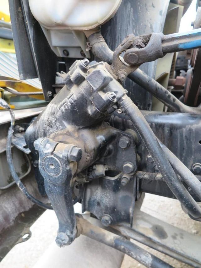 Vehicle component showing a hydraulic steering gearbox with linkages and hoses mounted on a truck chassis.