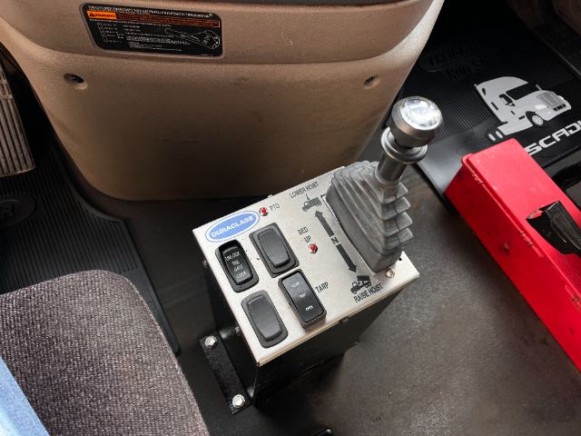 Truck interior showing a manual shifter with a Ram label and a control panel featuring buttons and a USB-like module, labeled with various indicators.