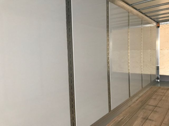 Interior of a trailer with vertical metal tracks and light-colored walls, wooden floor, and a metal roof.