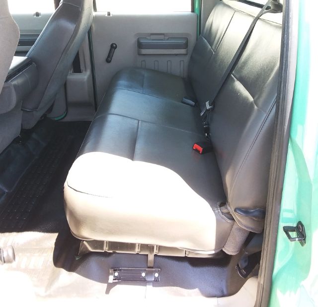 Ford F-250 interior: rear bench seat in a crew cab with black vinyl upholstery, light gray door panel, seatbelts visible, part of a flatbed truck.