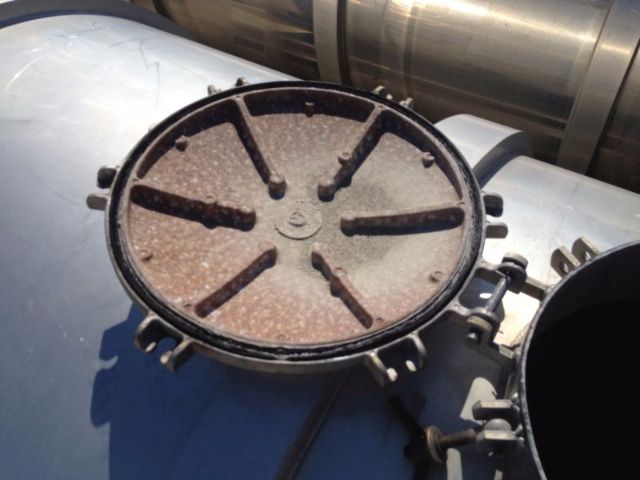Circular manhole-like lid on a vacuum tank with eight radial ribs and a central hub, rust color surface, on top of a metal cylindrical tank.