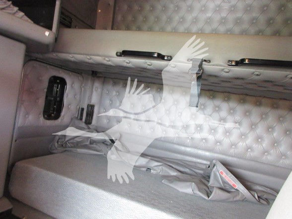Kenworth W900L sleeper cab interior; quilted grey side paneling with two vertical black handles and a small window/air vent; seatbelt and fabric trim visible.