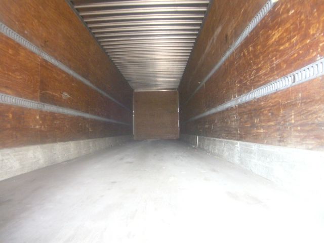 Interior of a trailer with wooden side walls and metal rails; empty cargo area with light shade at far end.