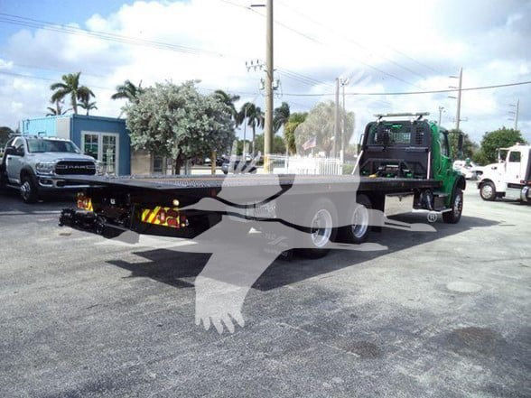 Flatbed trailer chassis attached to a Freightliner Business Class M2 106 truck in a parking lot.