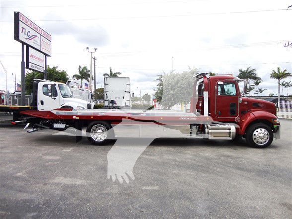 2022 Peterbilt 337 tow truck with red cab and flatbed, side view, stock sign in lot.