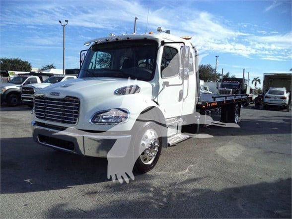 Tow truck (Freightliner BUSINESS CLASS M2 106 PLUS) white cab with flatbed in a dealership lot.