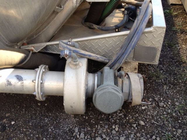 Vacuum tank truck rear wheel assembly with metal piping, hoses, and a gray circular access cap. Diamond plate toolbox visible in background.
