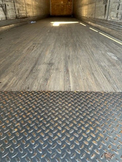 Trailer interior showing wooden side walls and a diamond plate steel threshold at the entry. Long empty cargo floor with light streaming in from rear opening.