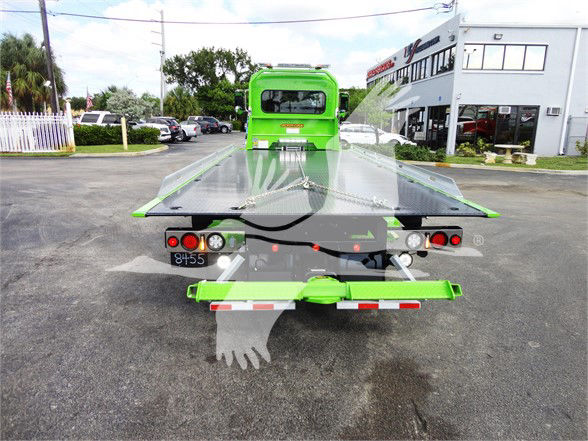Rear view of a bright green 2022 Peterbilt 337 tow truck with a flatbed in a dealership lot. Visible text includes license plate area and taillight panels.
